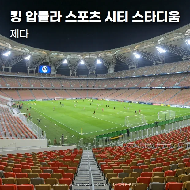 제다 킹 압둘라 스포츠 시티 스타디움의 야간 경기 전경. 조명이 켜진 흰 지붕 아래 빨강·주황·노랑 좌석이 그라운드를 둘러싸고 있습니다