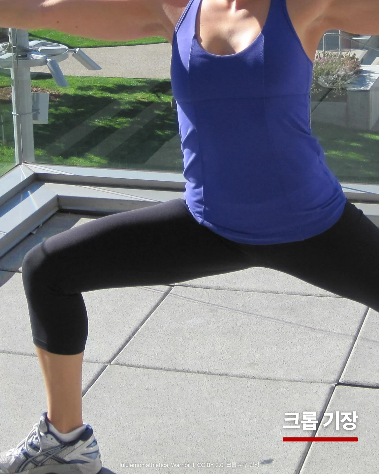 파란 탱크톱과 검은 크롭 레깅스를 입고 야외 테라스에서 워리어 II 자세를 한 사람의 몸통 아래를 담은 사진입니다. 앞으로 굽힌 다리의 레깅스 끝단이 종아리 중간에서 끝나고 그 아래로 맨 종아리와 운동화가 보이며, 오른쪽 아래 바닥 위에 '크롭 기장'이라는 글자가 놓여 있습니다.