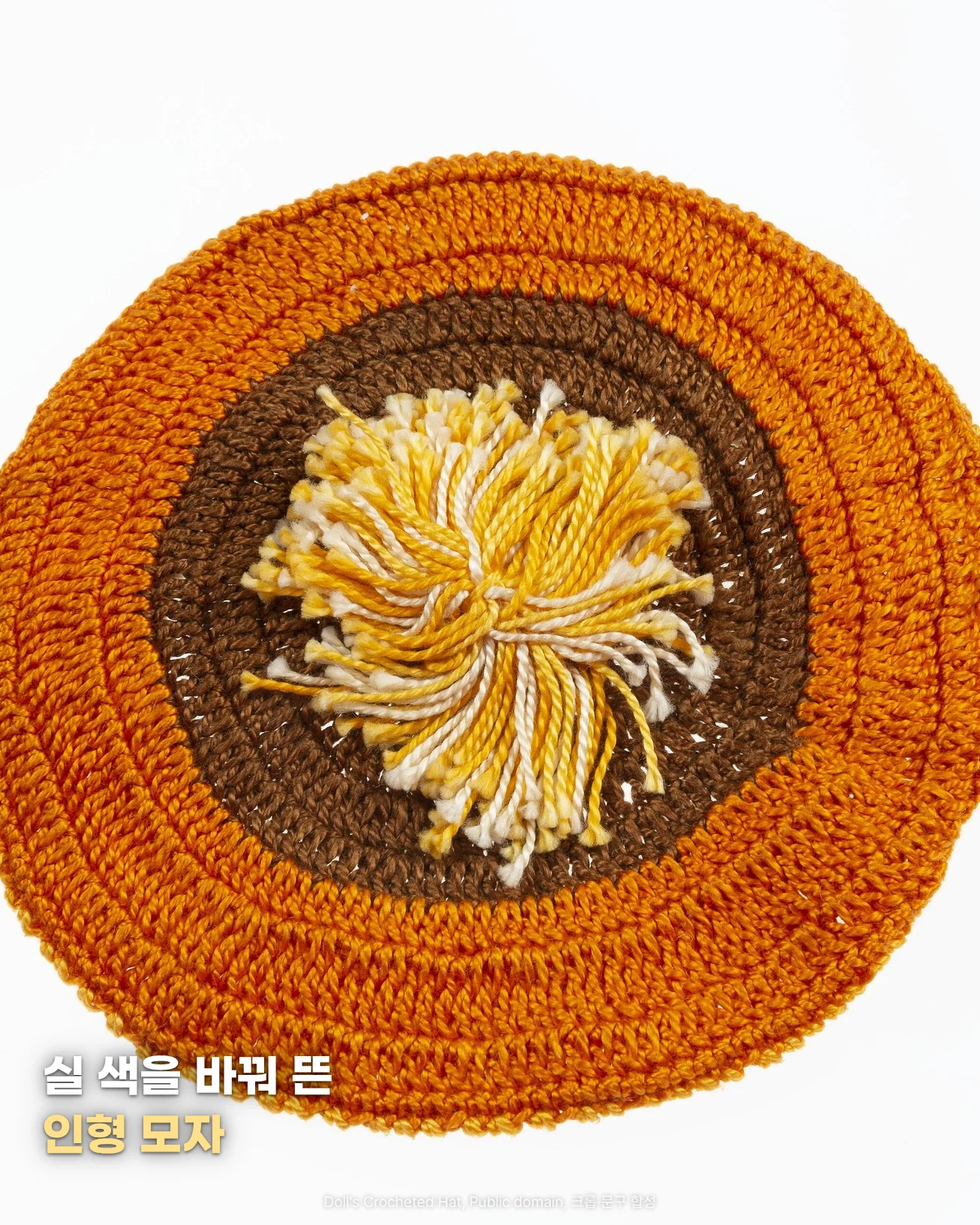 흰 바탕 위에 바깥은 주황색, 안쪽은 갈색으로 둥글게 뜬 인형 모자를 위에서 내려다본 사진, 가운데에 노란색과 흰색 실 술이 달려 있고 '실 색을 바꿔 뜬', '인형 모자' 문구가 있는 이미지