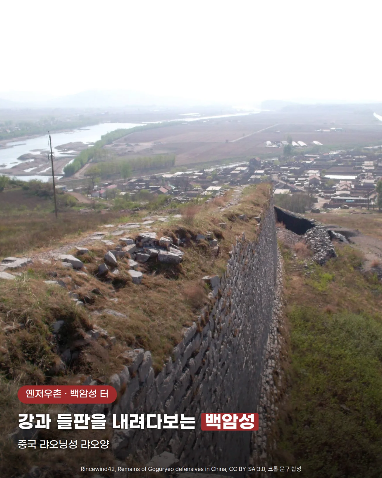 돌로 쌓은 백암성 성벽이 풀 덮인 언덕 능선을 따라 아래로 이어지고, 그 끝에 마을과 들판, 굽어 흐르는 강이 내려다보이는 사진. 아래쪽에 '옌저우촌 · 백암성 터' 배지와 '강과 들판을 내려다보는 백암성', '중국 랴오닝성 랴오양' 문구가 있다.