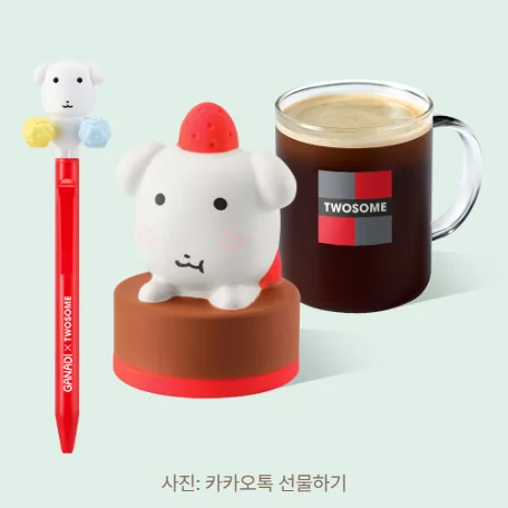 카카오톡 선물하기 상품 사진. 연한 민트색 바탕에 위쪽에 가나디와 노란·하늘색 폼폼 장식이 달린 빨간 GANADI × TWOSOME 응원 액션 볼펜, 딸기 모자를 쓰고 초코 케이크 받침 위에 앉은 가나디 스퀴시, TWOSOME 로고가 찍힌 유리잔 아메리카노 한 잔이 나란히 놓여 있습니다.