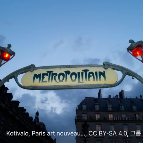 파리 지하철 입구의 아르누보 양식 'METROPOLITAIN' 간판과 그 양쪽에 붉은 등이 달린 녹색 철제 기둥을 아래에서 올려다본 사진입니다. 뒤로 구름 낀 저녁 하늘과 석조 건물이 보입니다.