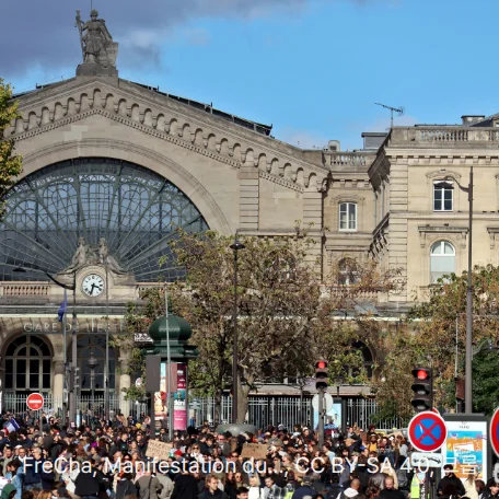 10월 17일 시위 당일 파리 동역(Gare de l'Est) 앞을 시위대가 메운 모습을 멀리서 찍은 사진입니다. 위쪽에 동역의 아치형 유리창과 석조 건물이 있고, 아래쪽에 많은 사람이 작게 모여 있으며, 오른쪽에 교통 표지와 신호등이 서 있습니다.