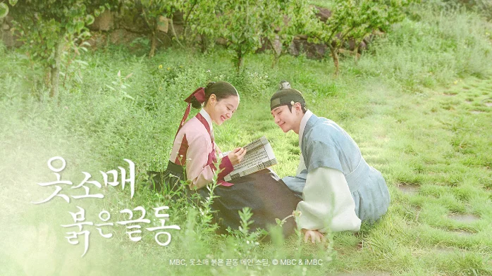 옷소매 붉은 끝동 공식 스틸. 한복 차림의 이준호와 이세영이 초록 풀밭에 나란히 앉아 웃으며 한 권의 책을 함께 읽고 있고, 왼쪽 아래에 흰 붓글씨 작품 제목이 있습니다