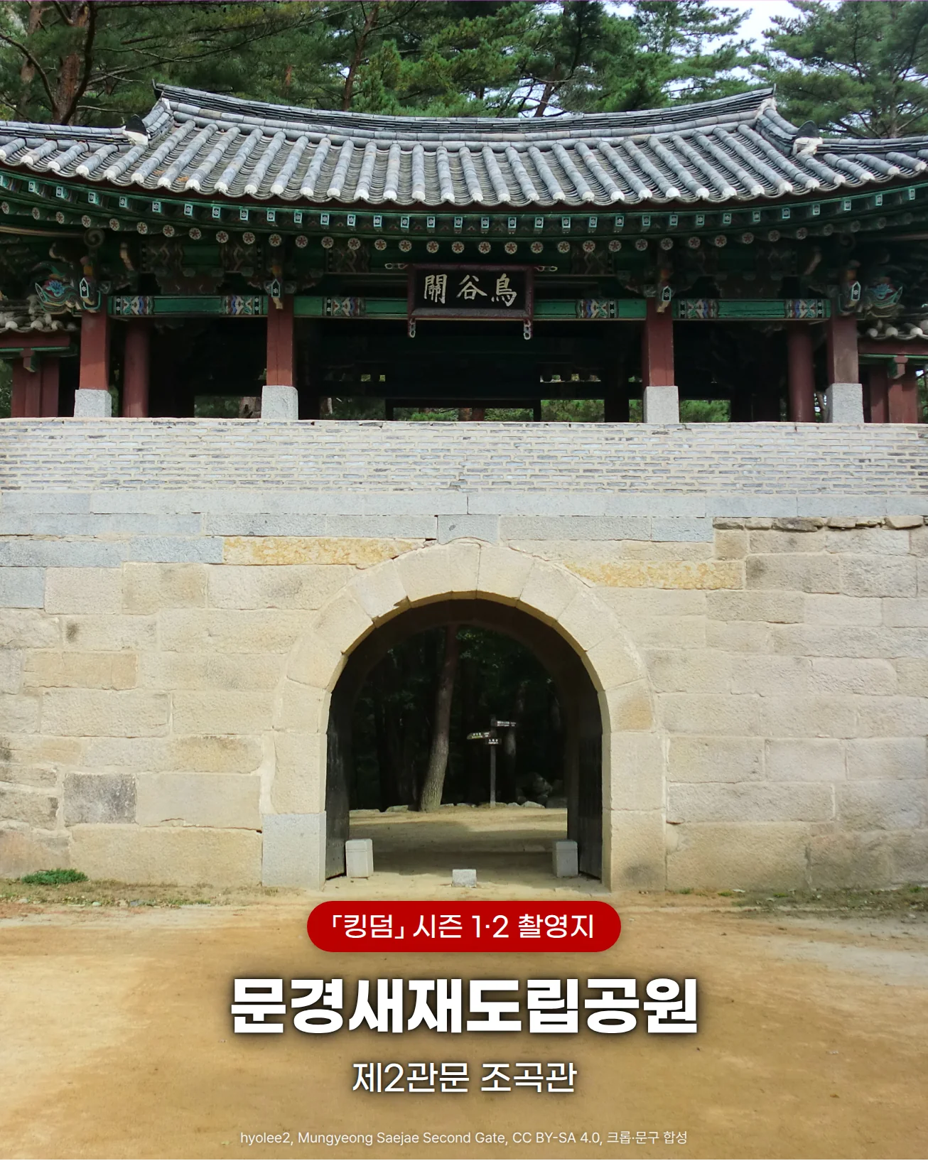 문경새재도립공원 제2관문 조곡관 사진. 소나무 숲 앞에 기와 문루를 얹은 돌 성벽과 아치형 성문이 있고 앞쪽에 넓은 흙길이 있으며, 흙길 위에 킹덤 시즌 1·2 촬영지, 문경새재도립공원, 제2관문 조곡관 문구가 있습니다