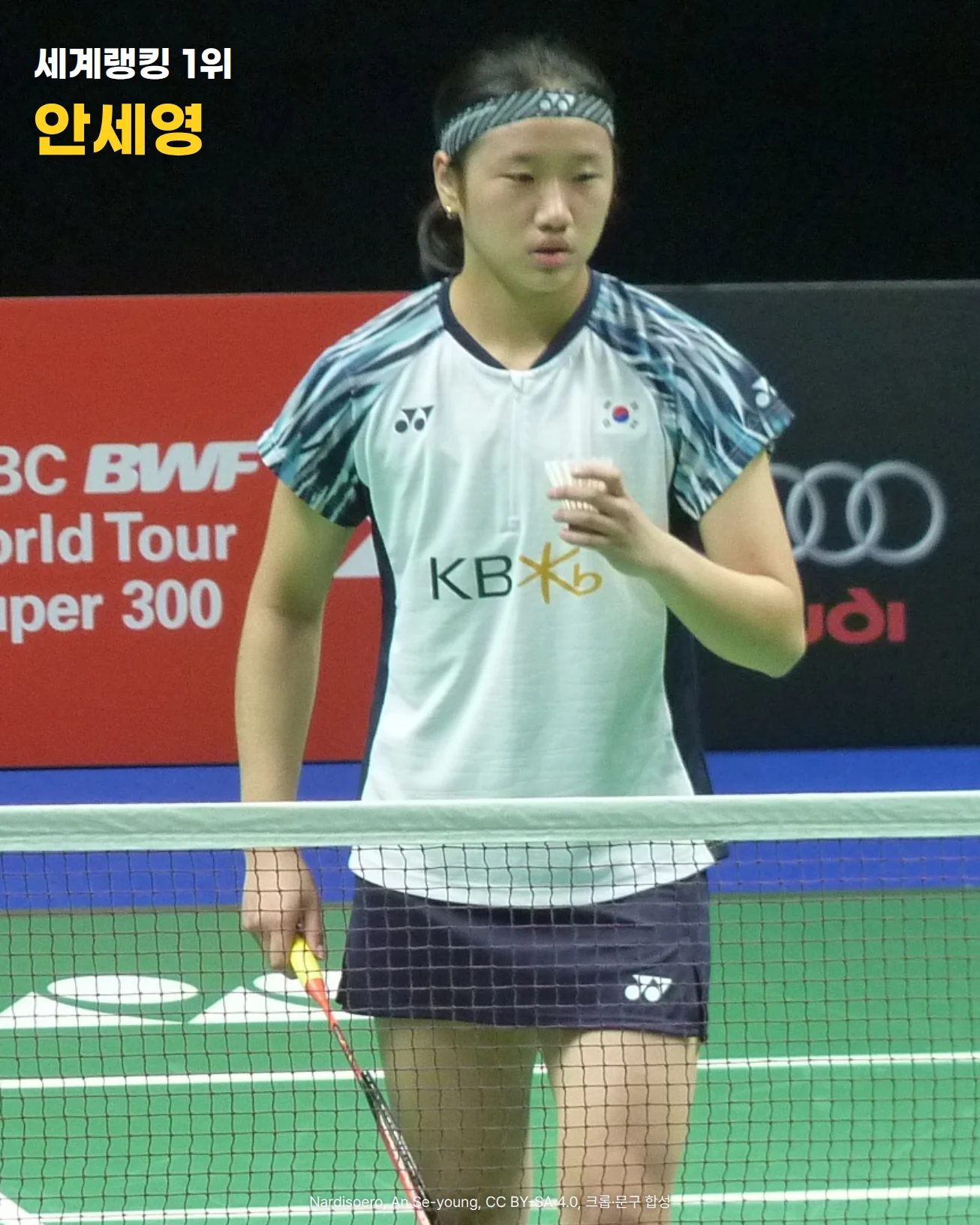 검은 배경과 'BWF World Tour' 광고판 앞, 초록 코트의 네트 뒤에 머리띠를 하고 태극기와 KB 로고가 있는 흰 경기복을 입은 안세영이 한 손에 셔틀콕, 다른 손에 라켓을 들고 서 있는 사진에 '세계랭킹 1위', '안세영' 문구가 있는 이미지
