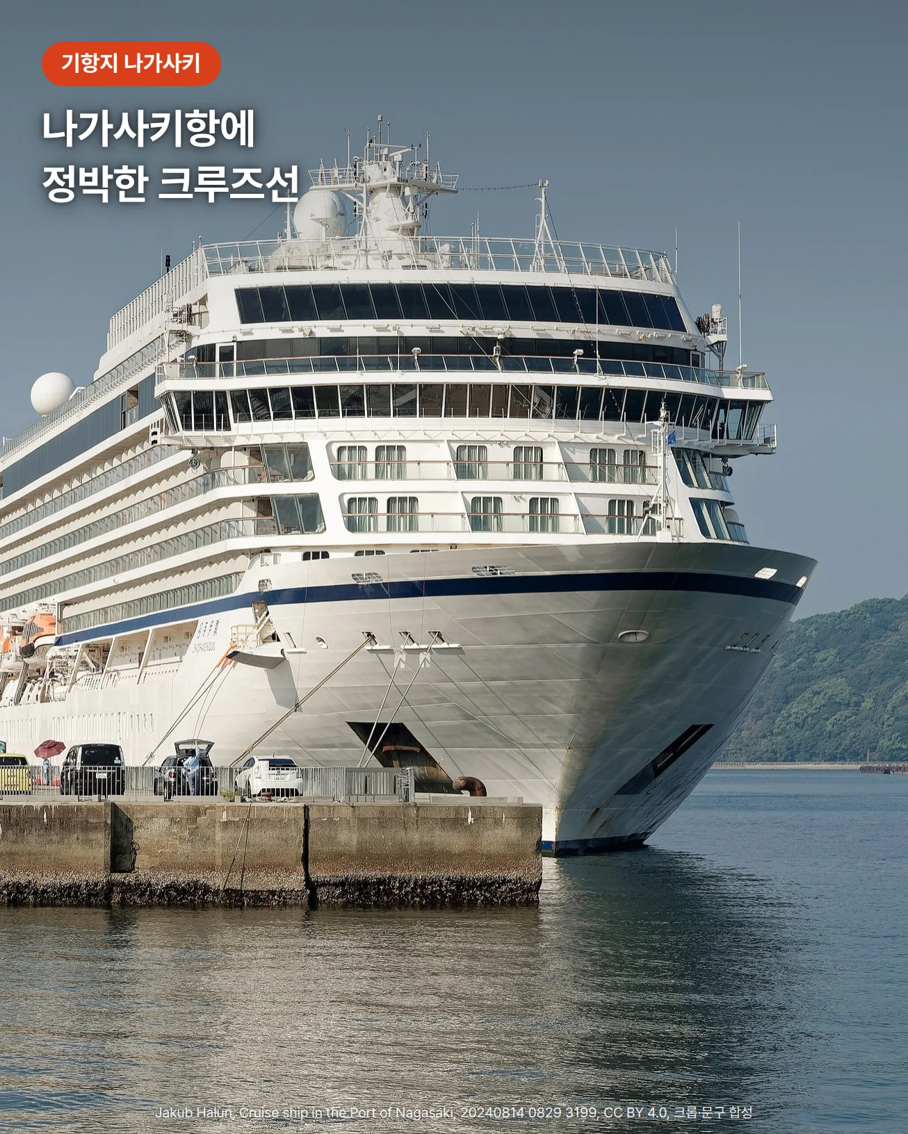 맑은 하늘 아래 나가사키항 부두에 정박한 흰색 대형 크루즈선을 앞쪽 비스듬한 각도에서 본 사진. 왼쪽에 항만 크레인과 건물, 오른쪽에 초록 언덕이 보이고, 위쪽에 '기항지 나가사키' 배지와 '나가사키항에 정박한 크루즈선' 문구