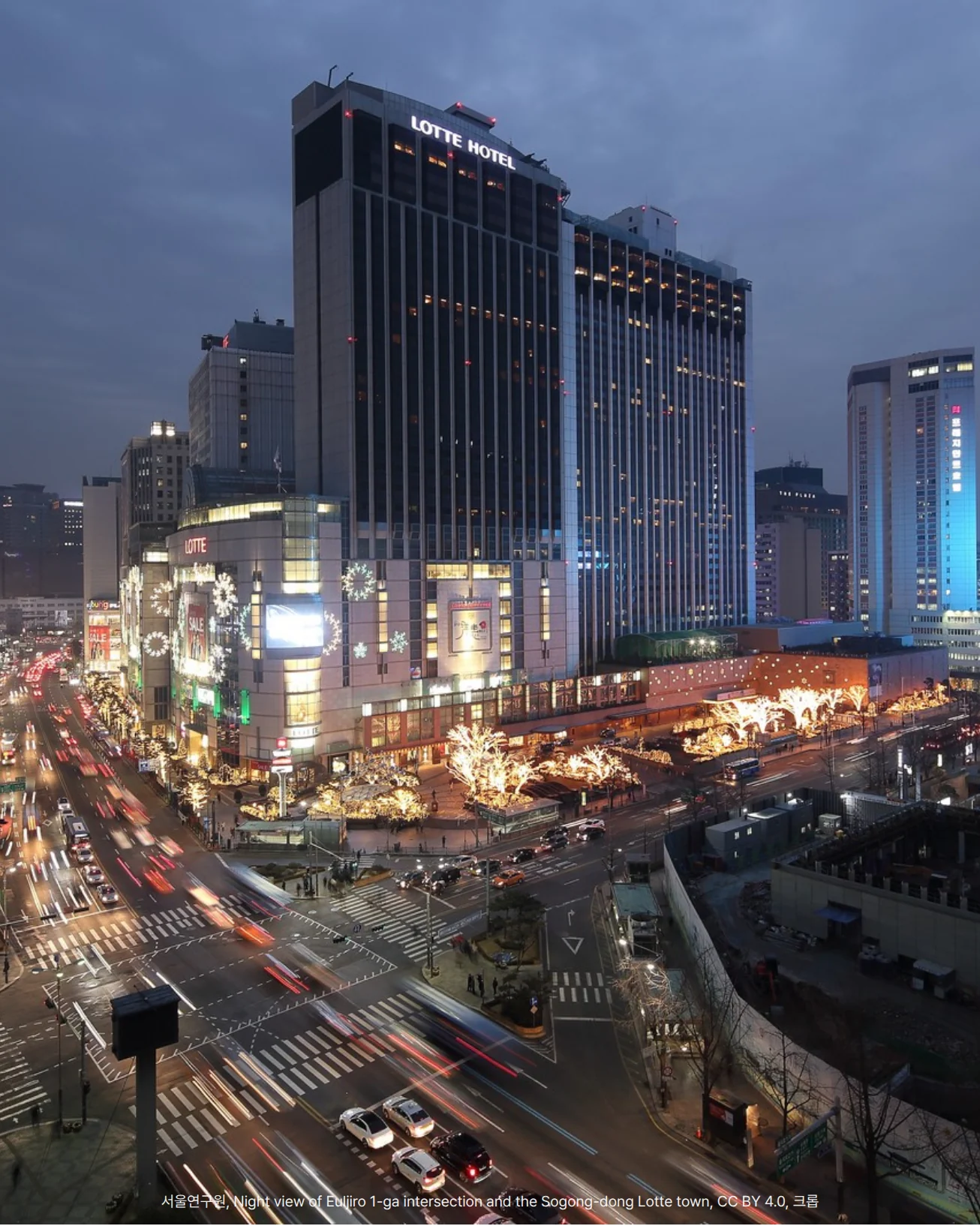 해 질 무렵 을지로 1가 교차로를 높은 곳에서 내려다본 야경 사진. 가운데에 'LOTTE HOTEL' 글자가 있는 고층 호텔 건물과 그 아래 조명 장식을 단 롯데백화점이 있고, 앞쪽 교차로에는 차량 불빛이 길게 이어집니다