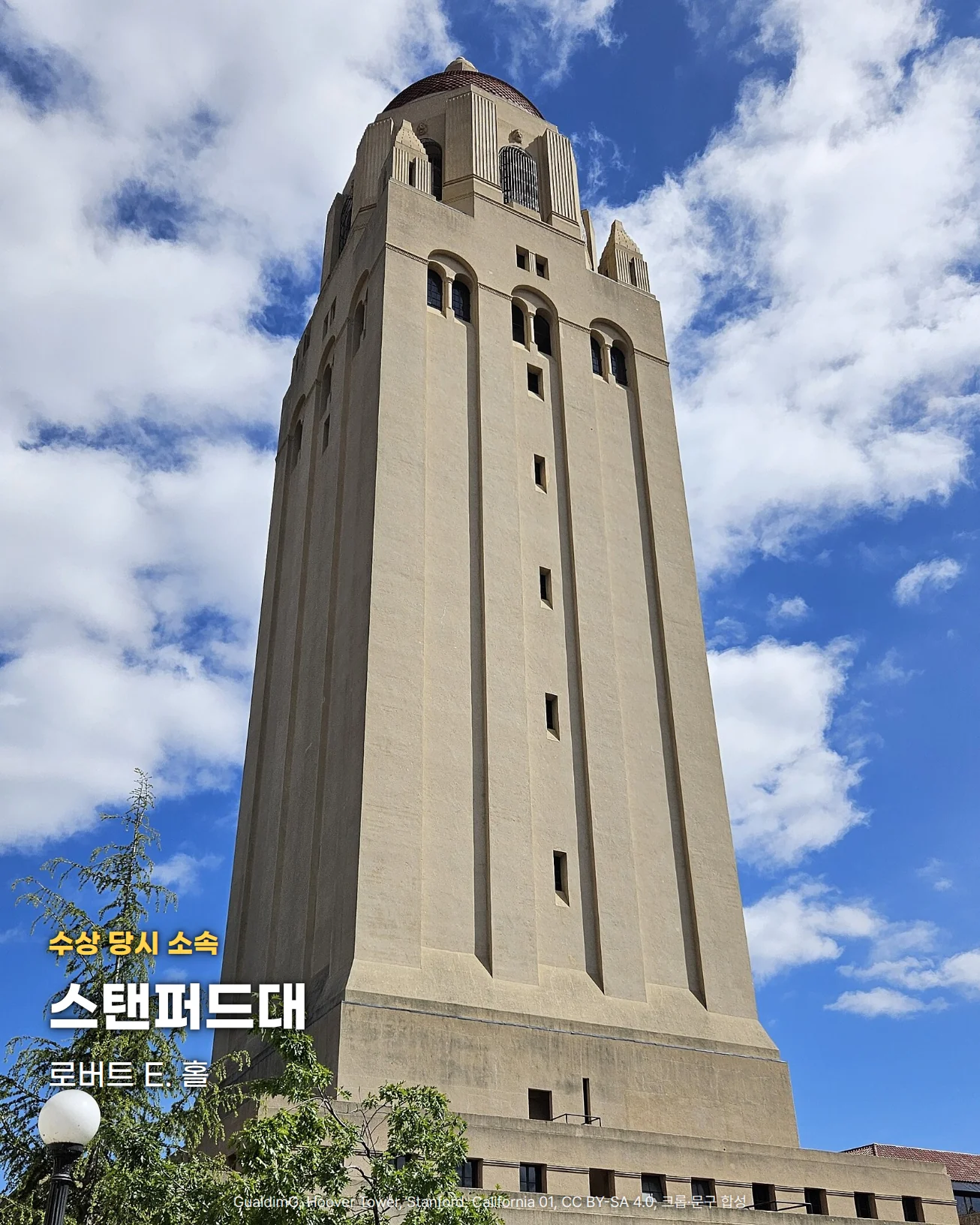 파란 하늘과 흰 구름을 배경으로 높이 솟은 연한 황갈색 석조 탑, 스탠퍼드대 캠퍼스의 후버 타워를 아래에서 올려다본 사진. 왼쪽 아래 나무와 가로등 위에 '수상 당시 소속', '스탠퍼드대', '로버트 E. 홀' 글자를 넣었습니다.