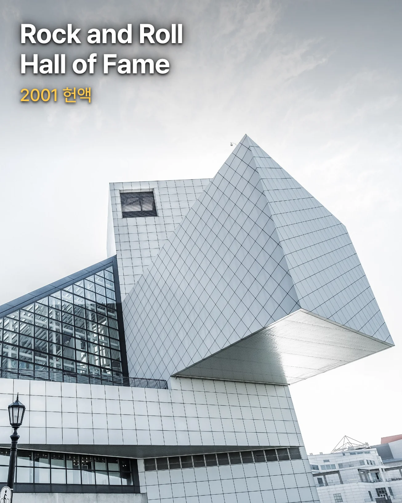 구름 낀 밝은 하늘 아래 비스듬한 유리 피라미드와 흰 타일 외벽의 타워가 이어진 클리블랜드 Rock and Roll Hall of Fame 건물을 아래에서 올려다본 사진 위에 「Rock and Roll Hall of Fame」과 「2001 헌액」 문구가 있습니다
