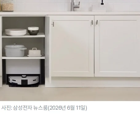 흰색 주방 하부장 한 칸의 문을 열어 둔 아래쪽에 삼성 비스포크 AI 스팀 로봇청소기와 스테이션이 들어가 있고 위 칸에는 그릇과 냄비가 놓인 모습