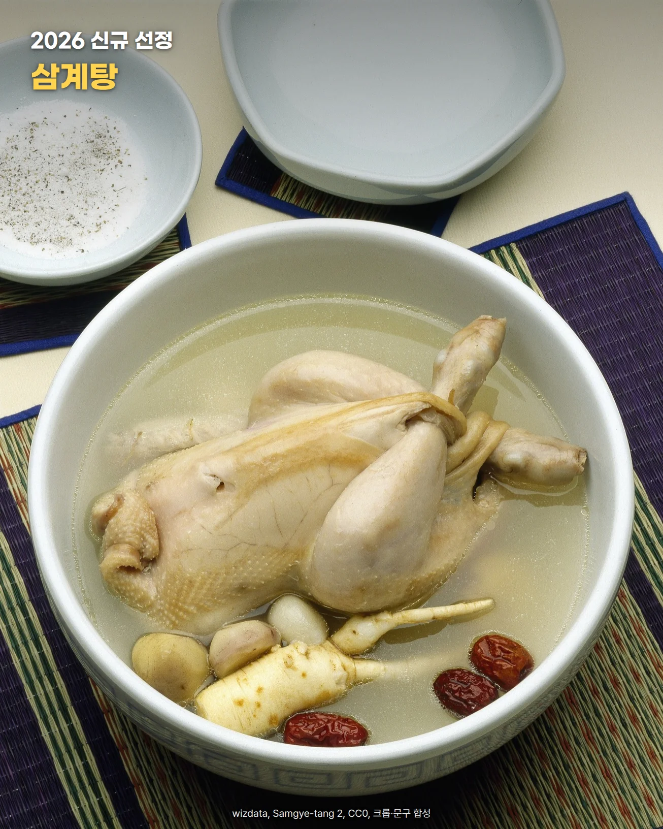 흰 사기그릇 맑은 국물에 통닭 한 마리가 잠겨 있고 앞쪽에 인삼과 대추가 보이는 삼계탕 한 그릇. 보라색 왕골 매트 위에 놓였고 뒤쪽에 소금 종지가 있다. 사진 위에 '2026 신규 선정, 삼계탕' 문구