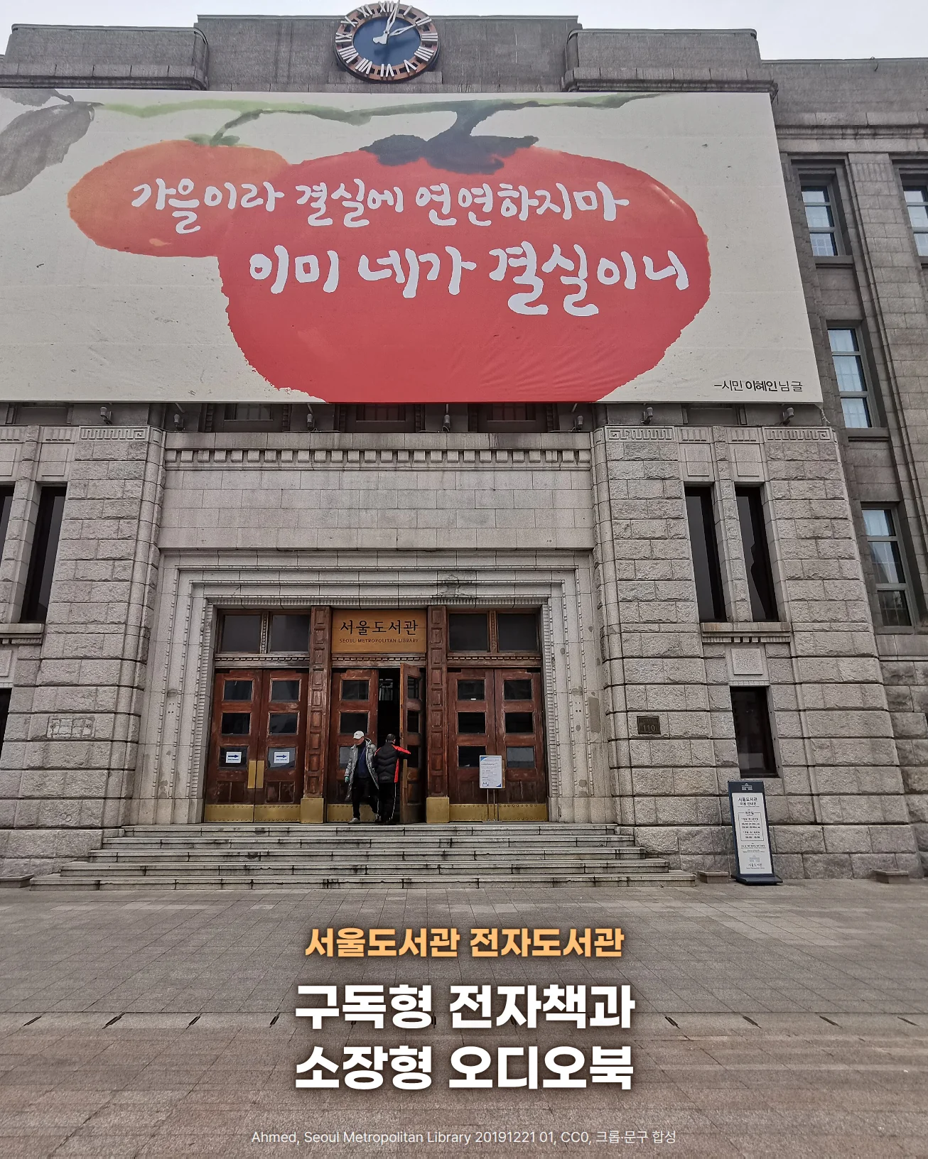 서울도서관 석조 건물을 정면에서 본 사진입니다. 시계탑 아래 감 그림과 '가을이라 결실에 연연하지마 이미 네가 결실이니' 글귀가 있는 대형 글판이 걸려 있고, 그 아래 '서울도서관' 현판이 달린 나무 정문과 계단, 앞 광장이 보입니다. 광장 위에 서울도서관 전자도서관, 구독형 전자책과 소장형 오디오북이라는 문구가 있습니다.