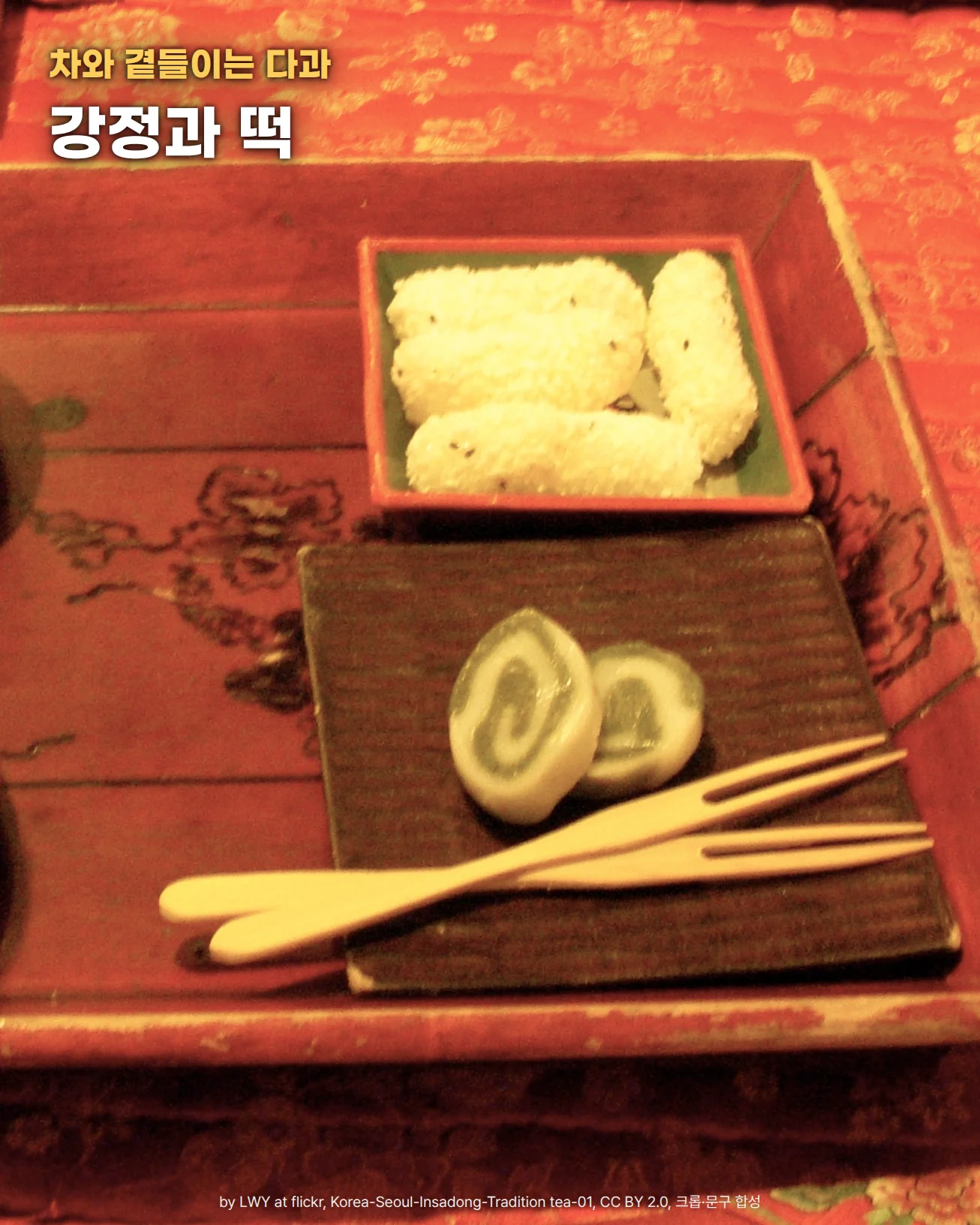 붉은 칠을 한 나무 쟁반 위에 초록 접시에 담긴 흰 강정 세 개와, 갈색 접시에 놓인 초록 소용돌이 무늬 떡 두 조각과 대나무 포크가 있고, 왼쪽 가장자리에 찻잔이 조금 보입니다. 쟁반 아래로 꽃무늬 붉은 상보가 깔려 있습니다. 위쪽에 차와 곁들이는 다과, 강정과 떡이라는 문구가 있습니다
