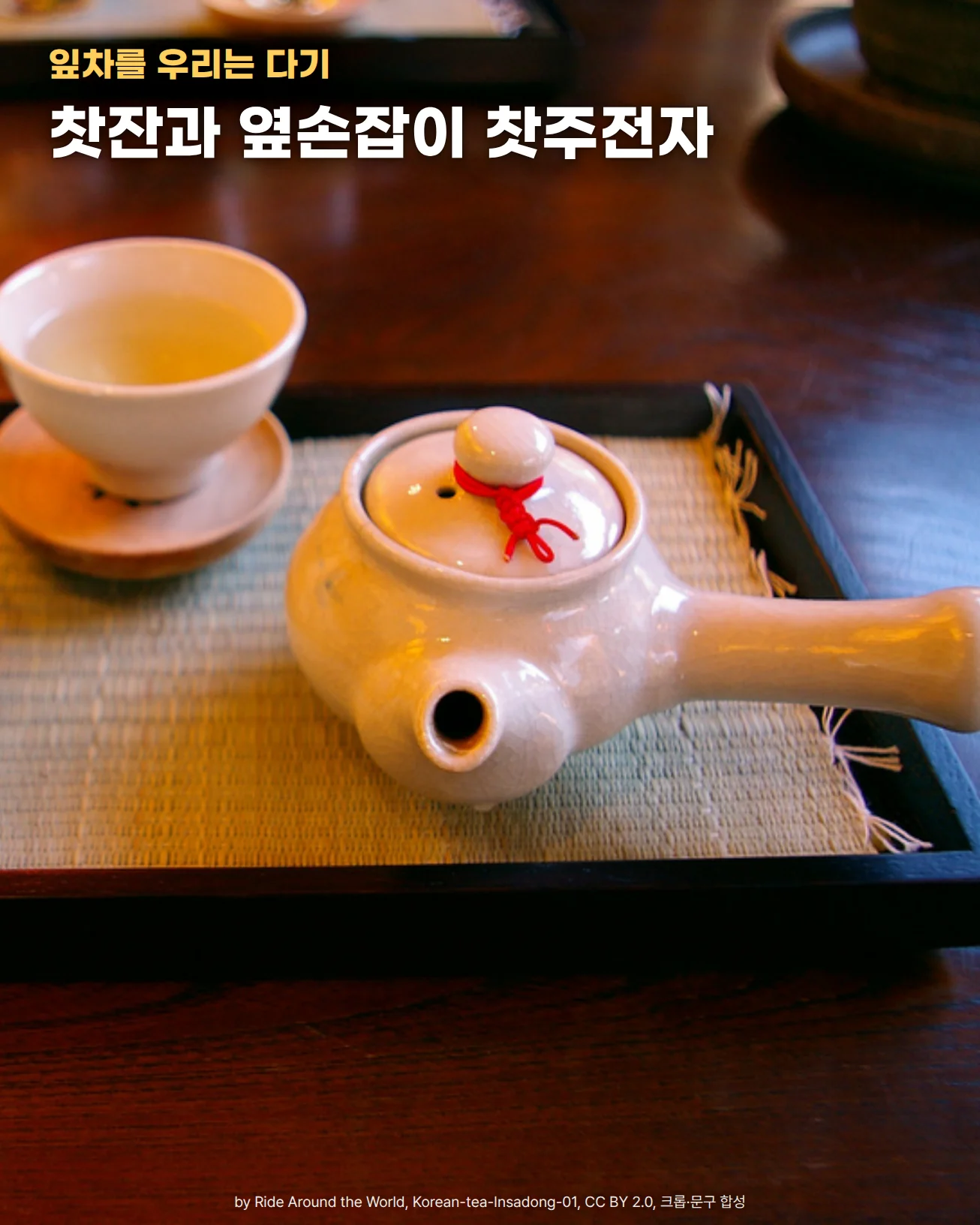짙은 나무 탁자 위 검은 쟁반에 대나무 받침이 깔려 있고, 그 위에 연한 차가 담긴 흰 찻잔이 나무 잔받침에 놓여 있습니다. 오른쪽에는 뚜껑 꼭지에 붉은 끈을 묶은 옆손잡이 흰 찻주전자가 있습니다. 위쪽에 잎차를 우리는 다기, 찻잔과 옆손잡이 찻주전자라는 문구가 있습니다